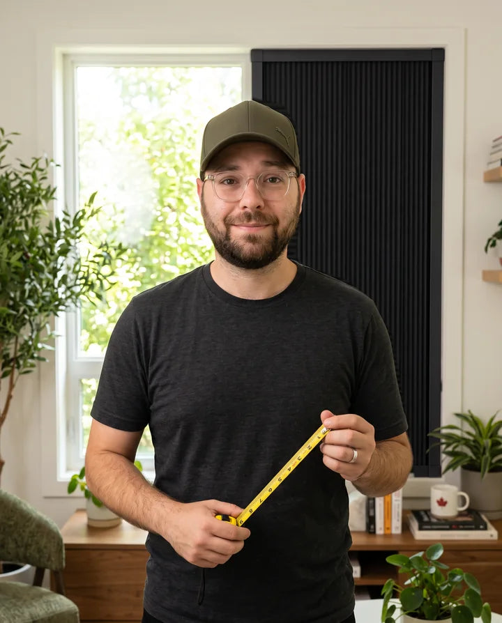 Charlie, Lights Out co-founder, holding a tape measure beside a blackout blind