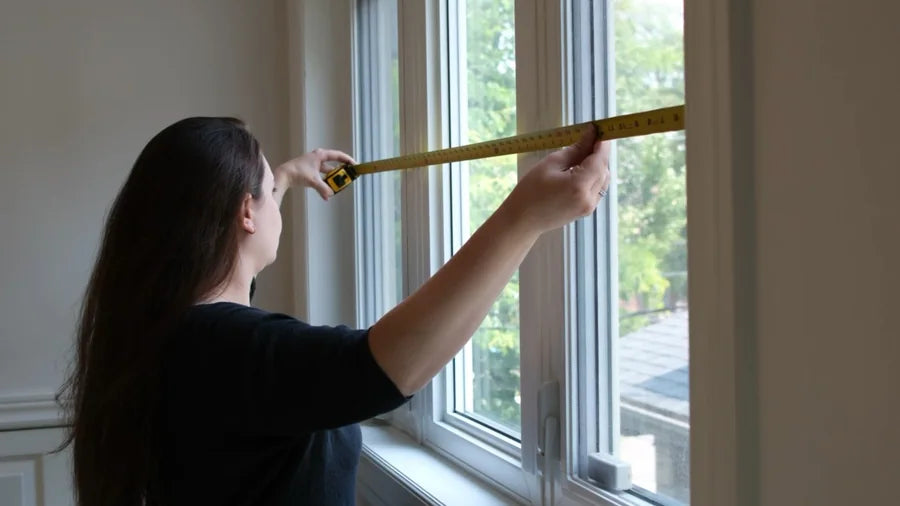 A woman extending a tape measure across the inside width of a window